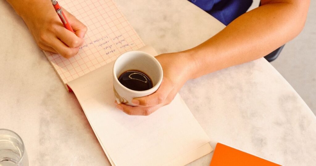 mulher escrevendo afirmações positivas em um caderno enquanto toma café pela manhã